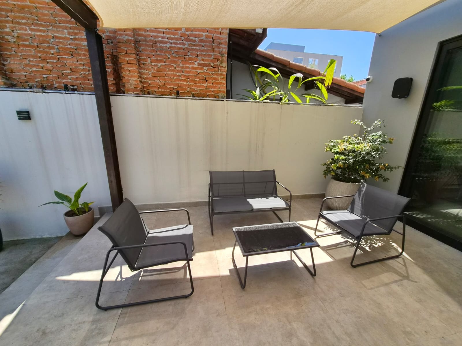 Conjunto de poltronas no estar externo, com planta em vaso e muro de tijolos