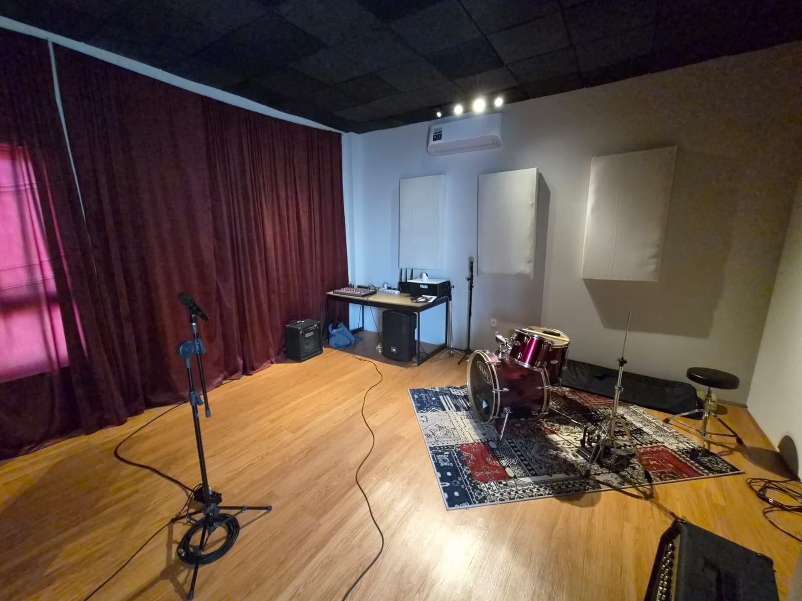 Estúdio musical com tratamento acústico, cortinas pesadas, bateria e piso de madeira
