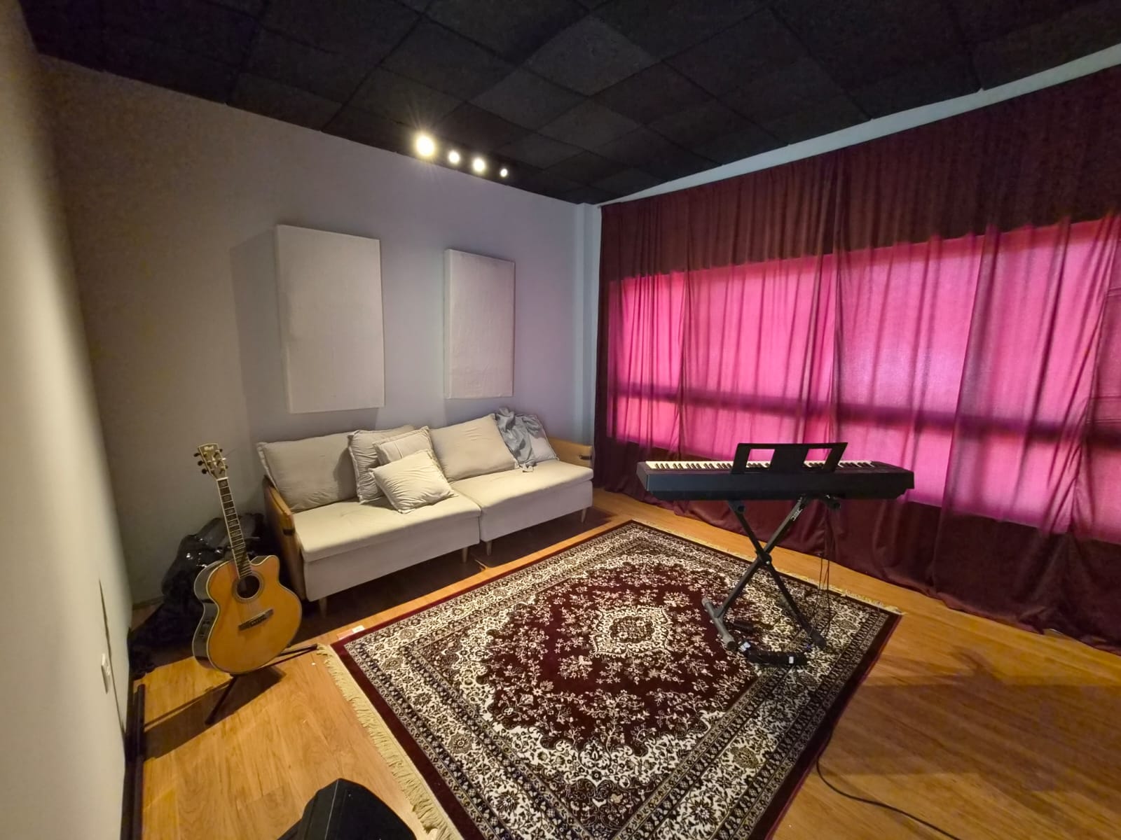 Estúdio com sofá, violão, teclado e cortinas