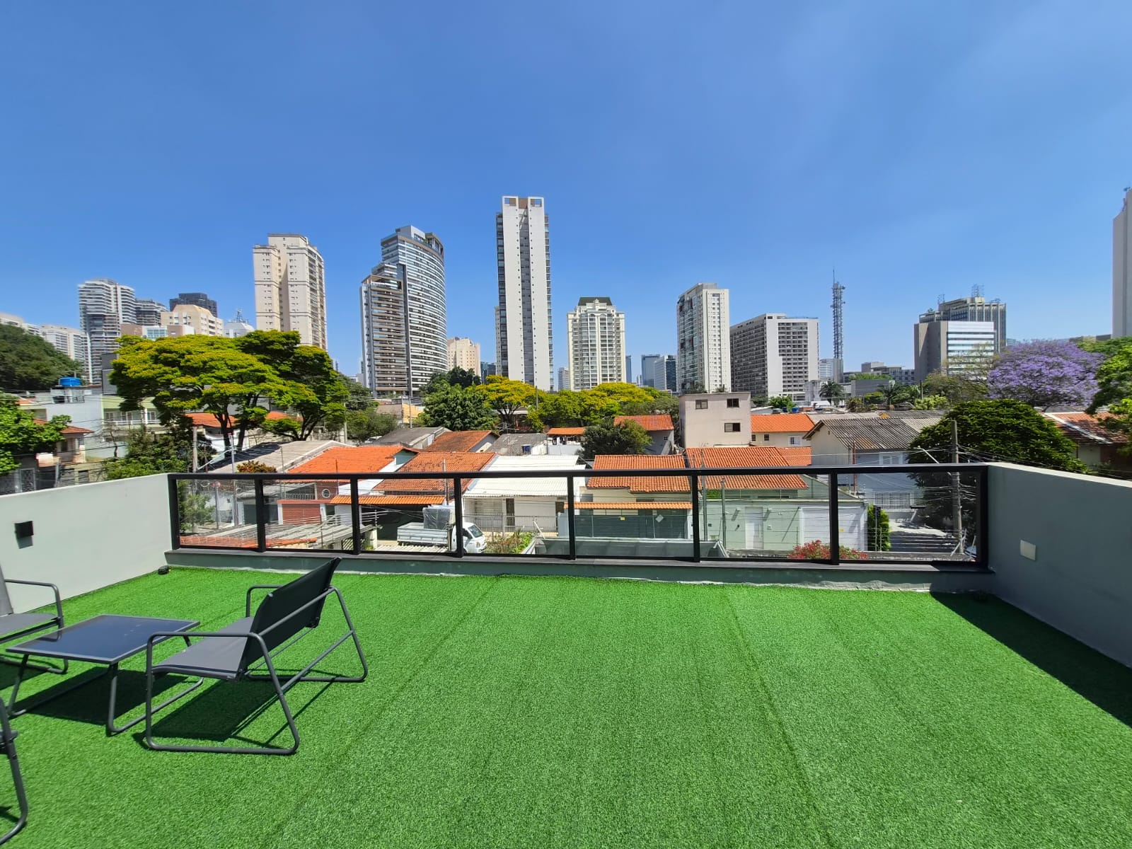 Terraço com grama sintética, cadeiras e vista aberta para os prédios da cidade